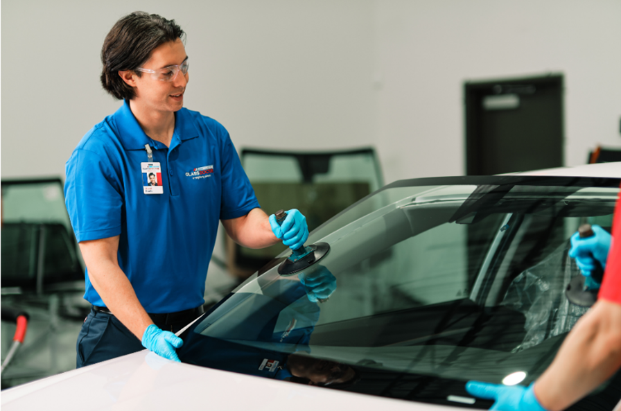 a male Glass Doctor service professional installing a windshield onto a white car with a suction cup